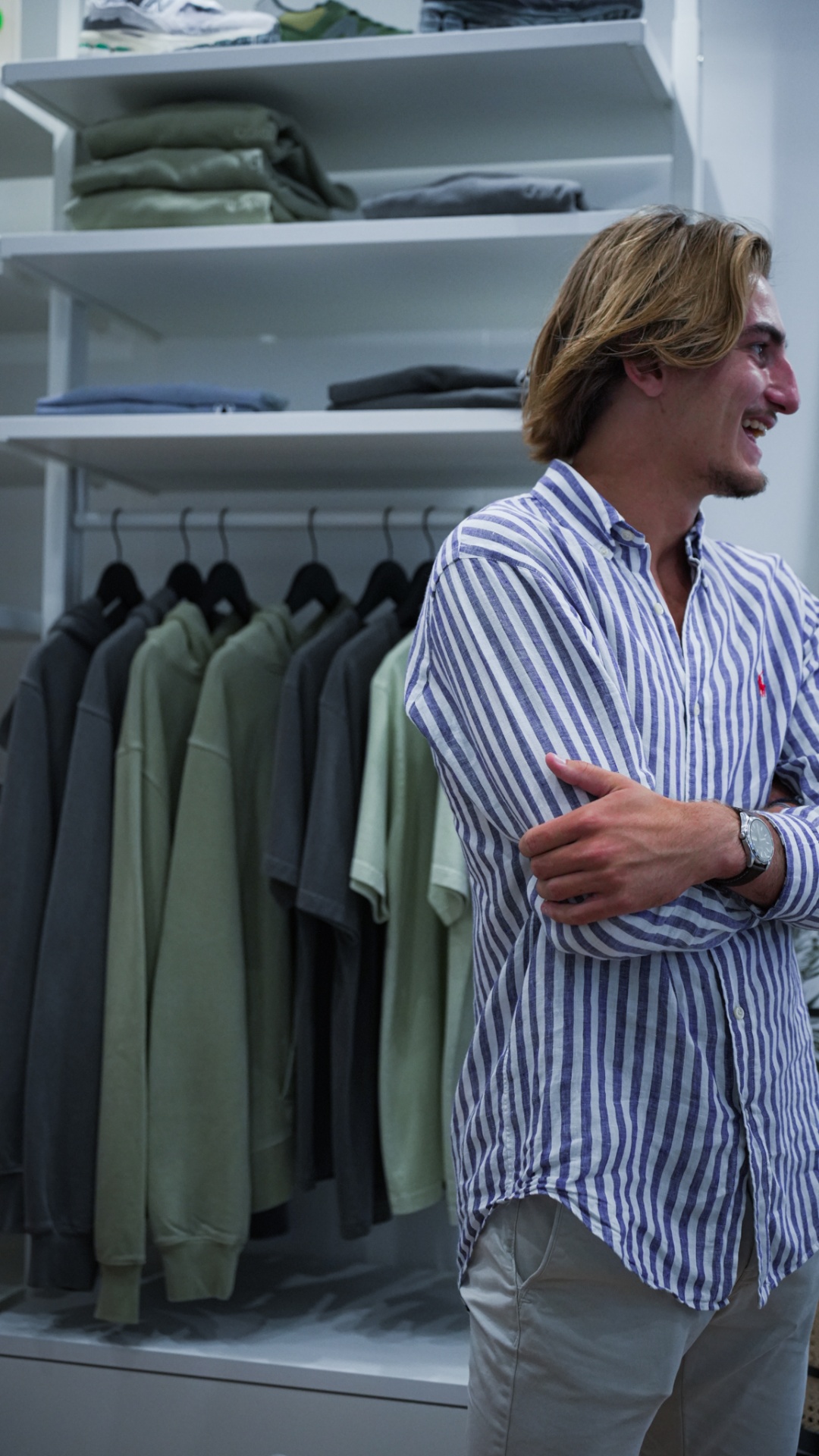 Client souriant en chemise rayée devant un rayon de vêtements