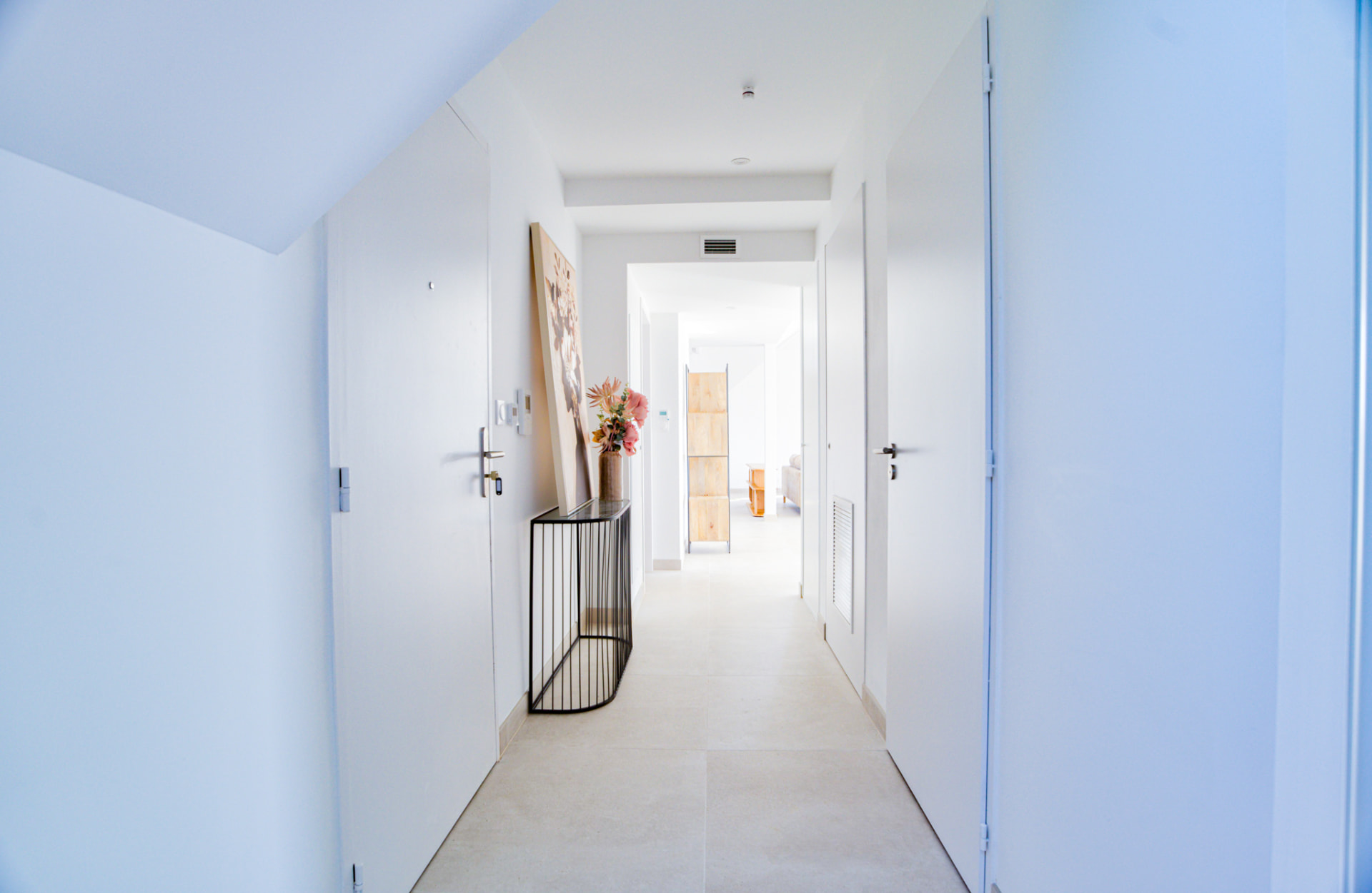 Couloir blanc desservant les pièces avec console et vase fleuri